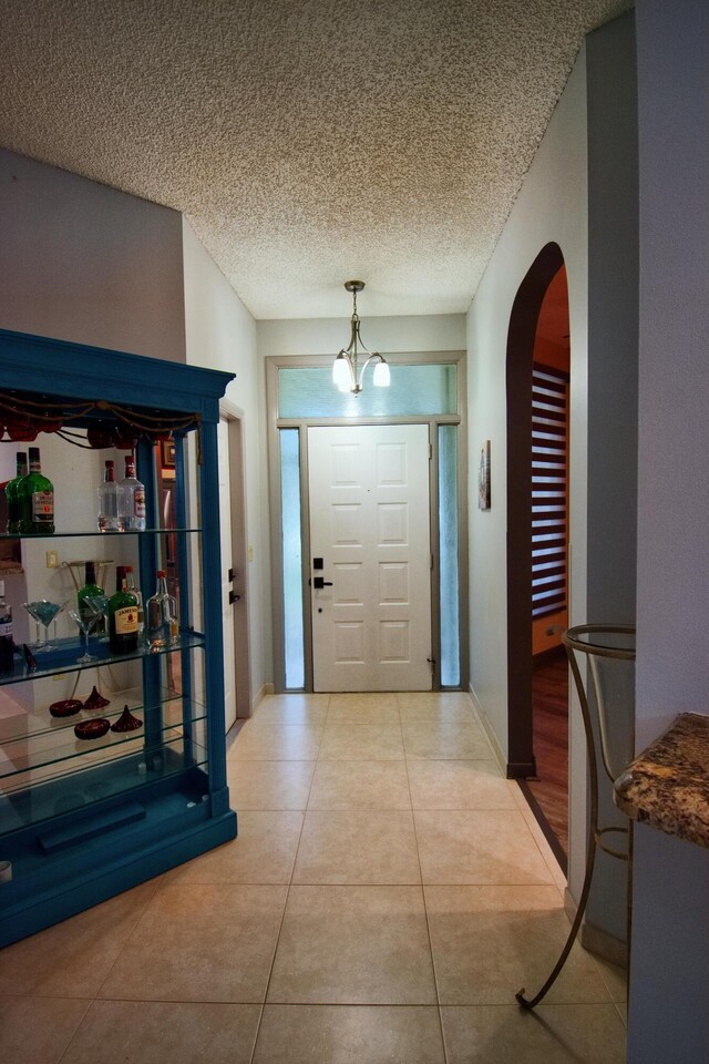 tiled entrance foyer featuring a notable chandelier and a textured ceiling