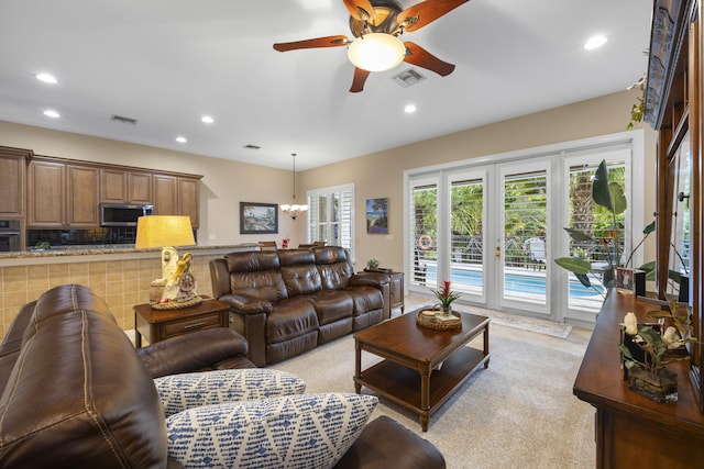 living room with ceiling fan with notable chandelier and light colored carpet