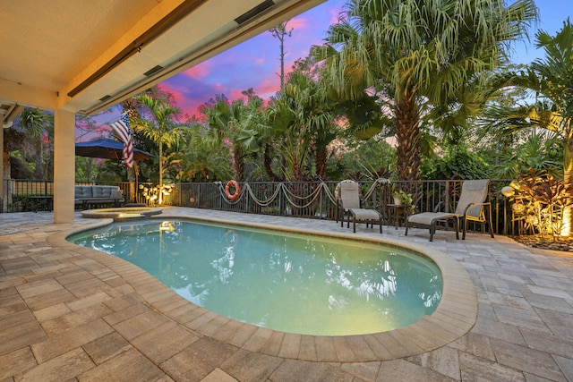 pool at dusk featuring a patio area and an in ground hot tub