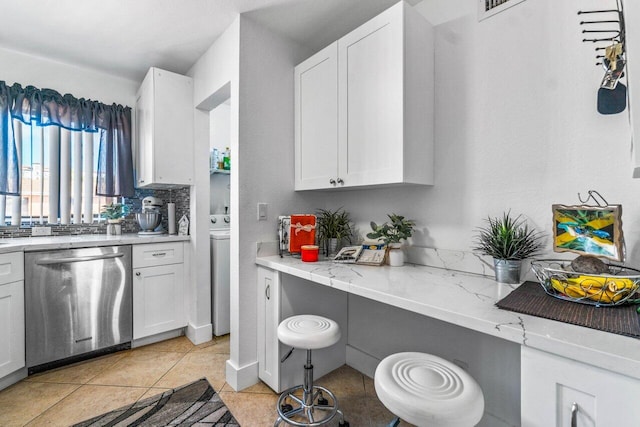 kitchen featuring white cabinets, light tile patterned floors, light stone counters, washer / clothes dryer, and stainless steel dishwasher