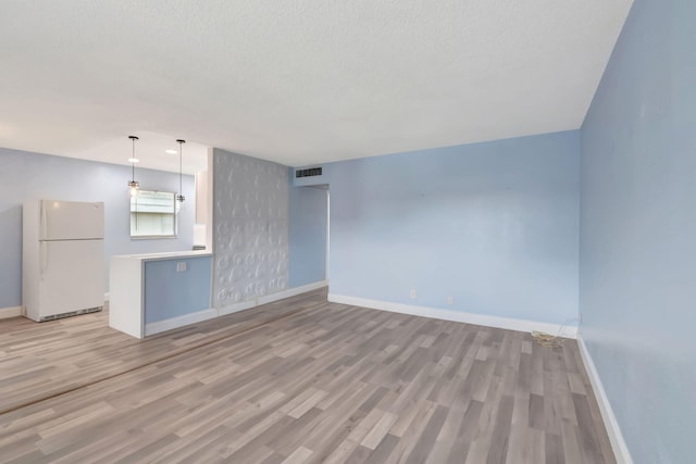 unfurnished living room with a textured ceiling and light hardwood / wood-style floors