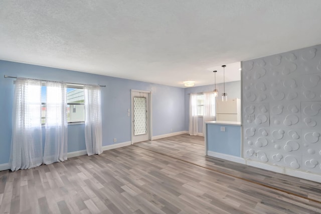 unfurnished living room featuring a textured ceiling, light wood-type flooring, and plenty of natural light