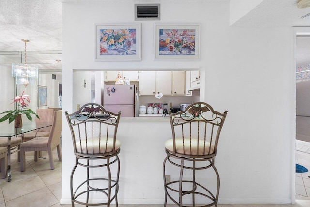 kitchen featuring white fridge, a textured ceiling, light tile patterned floors, kitchen peninsula, and white cabinets