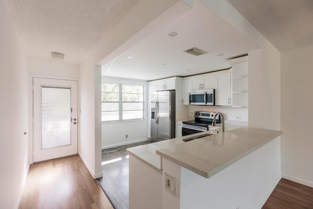 kitchen with light stone counters, stainless steel appliances, kitchen peninsula, and white cabinetry