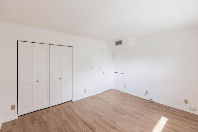 unfurnished bedroom with a textured ceiling, a closet, and light hardwood / wood-style flooring