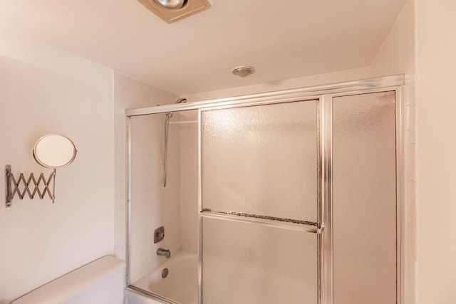 bathroom with toilet and combined bath / shower with glass door