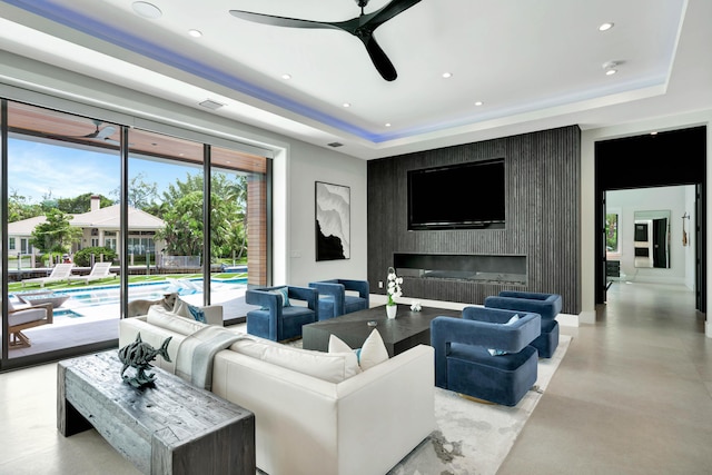 living area with a tray ceiling, a ceiling fan, recessed lighting, concrete floors, and an accent wall