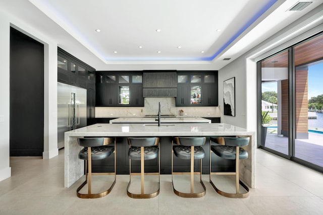 kitchen featuring stainless steel built in fridge, tasteful backsplash, a large island with sink, and plenty of natural light
