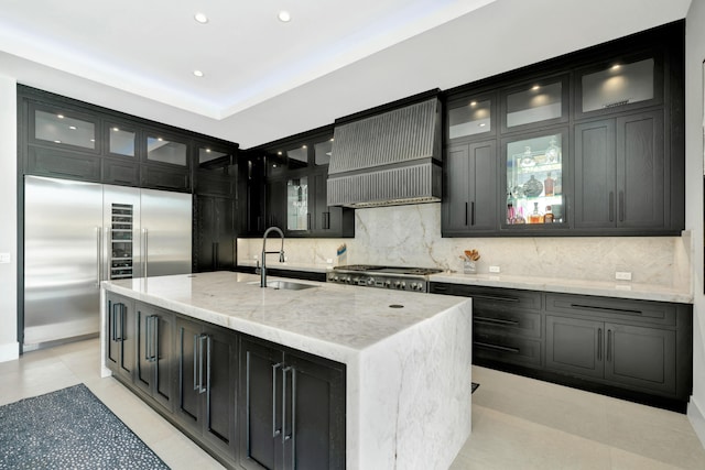 kitchen featuring appliances with stainless steel finishes, tasteful backsplash, an island with sink, sink, and custom exhaust hood