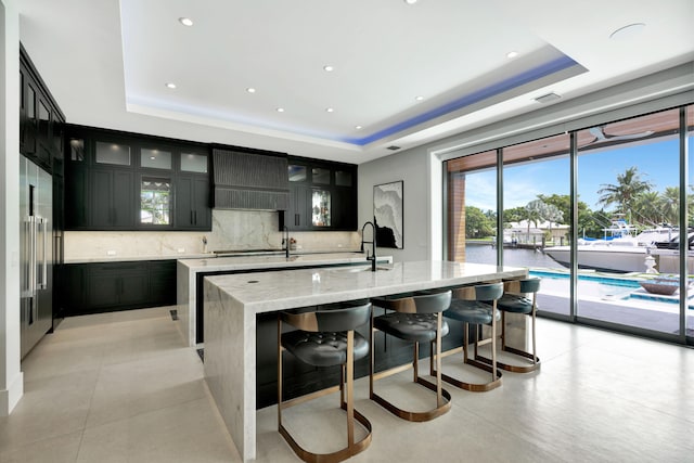 kitchen featuring a kitchen island with sink, custom range hood, and a tray ceiling