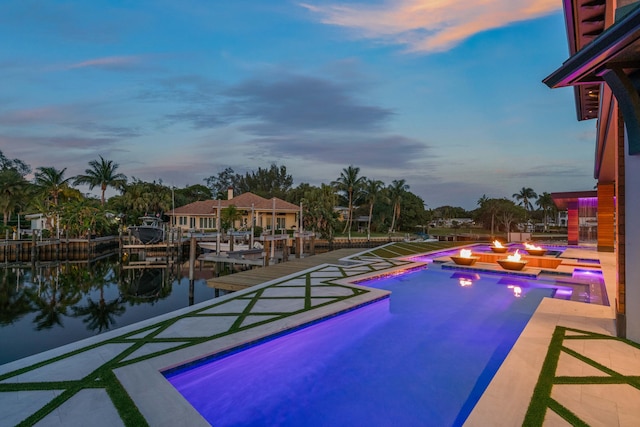 pool at dusk with a water view, a dock, and a patio