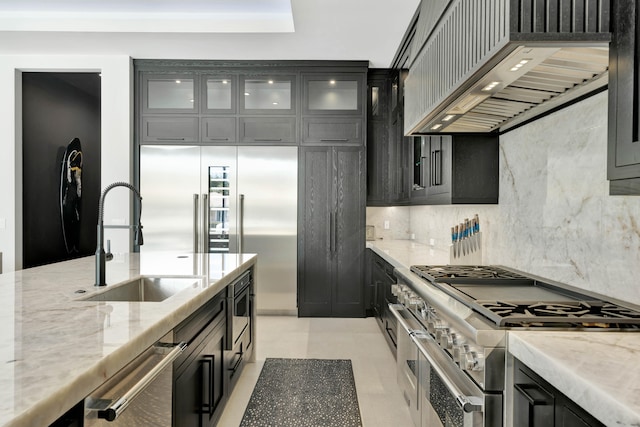 kitchen featuring tasteful backsplash, sink, premium range hood, light stone countertops, and premium appliances