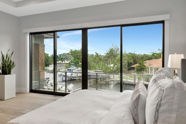 bedroom with a water view, multiple windows, light wood-type flooring, and access to outside