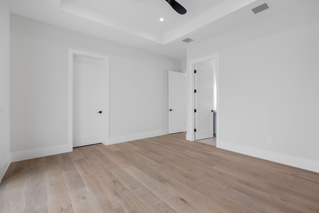 empty room with a raised ceiling, light hardwood / wood-style flooring, and ceiling fan