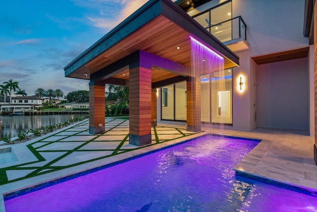 pool at dusk featuring a water view and a patio