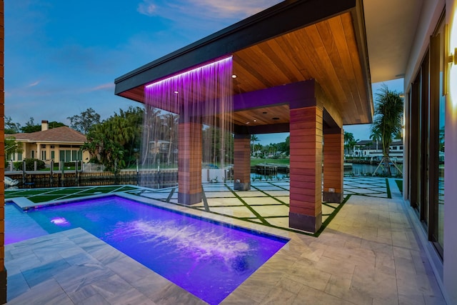 pool at dusk featuring a patio area and a water view