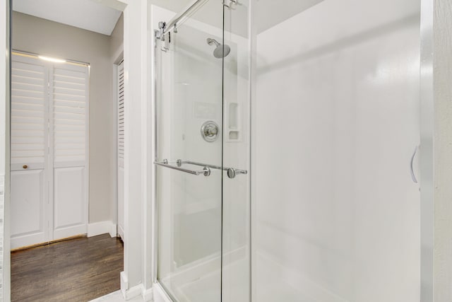 full bathroom featuring a stall shower, a closet, baseboards, and wood finished floors