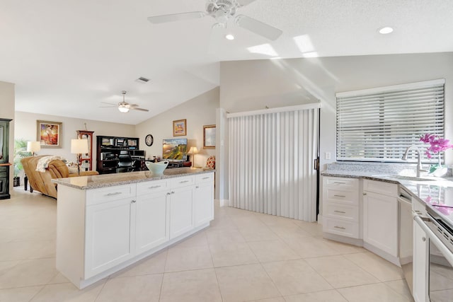 kitchen featuring vaulted ceiling, stainless steel stove, light tile patterned floors, ceiling fan, and white cabinets