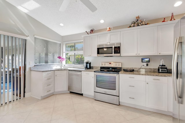 kitchen featuring vaulted ceiling, light tile patterned floors, stainless steel appliances, white cabinetry, and ceiling fan