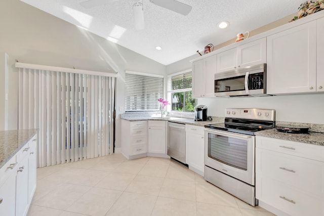 kitchen with a textured ceiling, vaulted ceiling with skylight, stainless steel appliances, white cabinetry, and ceiling fan