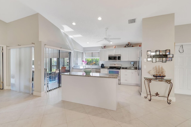 kitchen with a kitchen island, stone countertops, stainless steel appliances, ceiling fan, and white cabinets