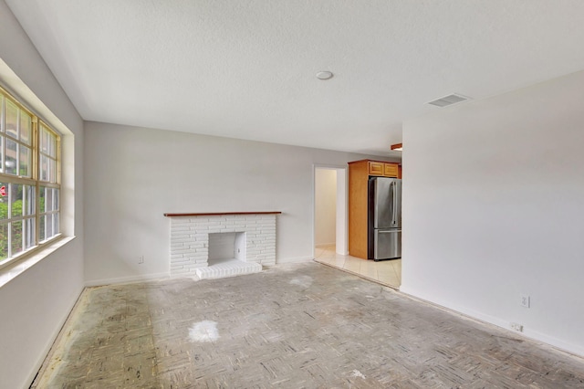 unfurnished living room featuring a brick fireplace, a textured ceiling, and light parquet floors