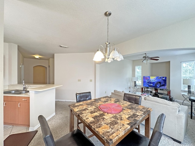 dining space with a textured ceiling, baseboards, visible vents, light carpet, and ceiling fan with notable chandelier