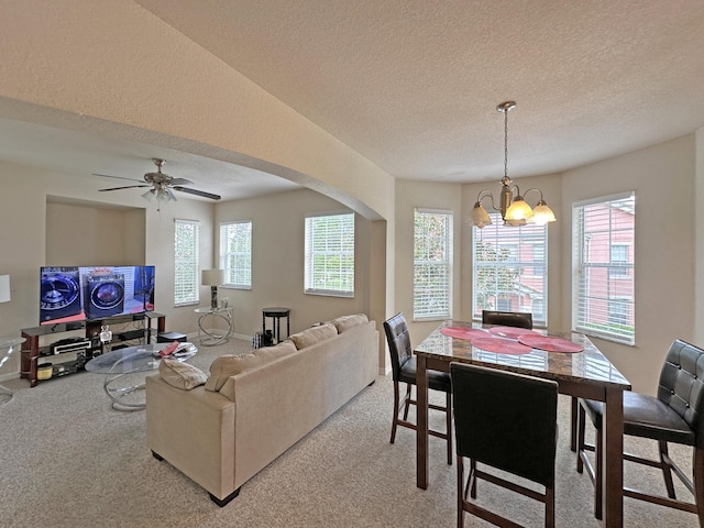 dining area with light carpet, plenty of natural light, ceiling fan with notable chandelier, and a textured ceiling