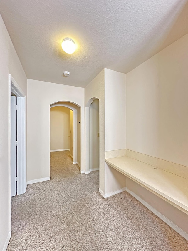 hall with baseboards, arched walkways, a textured ceiling, and carpet flooring