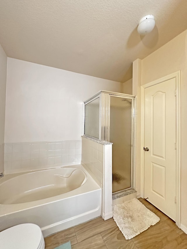 bathroom with a bath, a stall shower, toilet, and wood finished floors