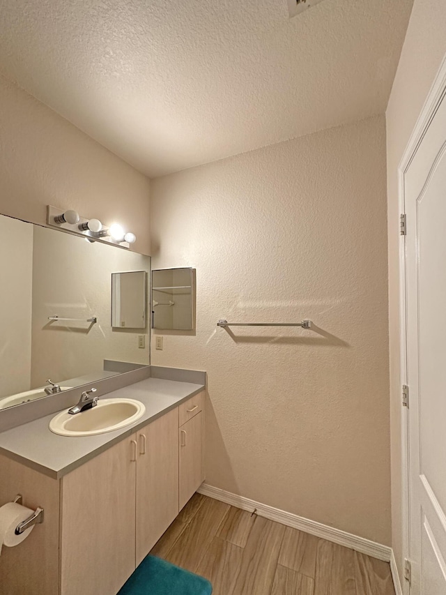 bathroom with vanity, wood finished floors, a textured wall, and a textured ceiling