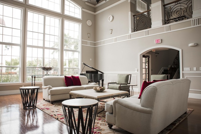 living area with arched walkways, wood finished floors, a towering ceiling, and a decorative wall