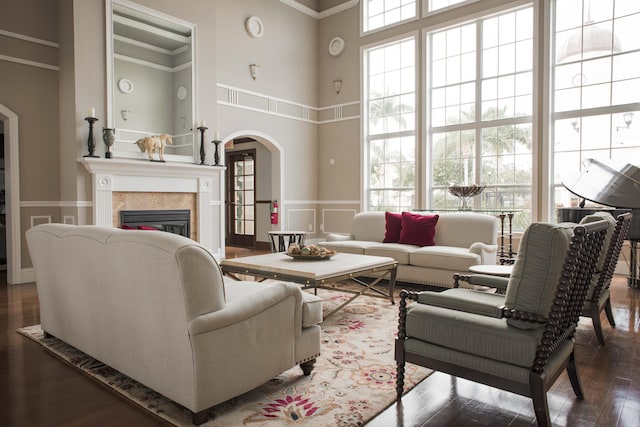 living area featuring a high ceiling, arched walkways, dark wood-style flooring, a glass covered fireplace, and a decorative wall