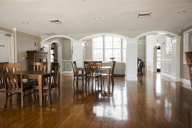 dining room with dark wood-style floors, visible vents, a decorative wall, and ornamental molding