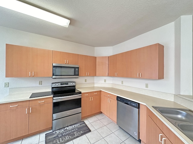 kitchen with light tile patterned floors, a sink, stainless steel appliances, light countertops, and a textured ceiling