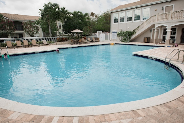 community pool featuring stairs, a patio, and fence