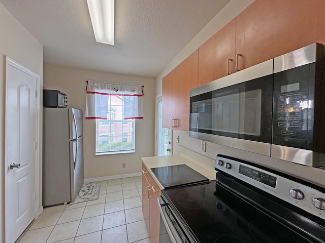 kitchen with a textured ceiling, stainless steel appliances, light countertops, light tile patterned floors, and baseboards