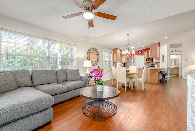 living room with light wood-type flooring, ceiling fan with notable chandelier, and a textured ceiling