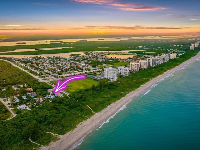 aerial view at dusk featuring a water view and a beach view