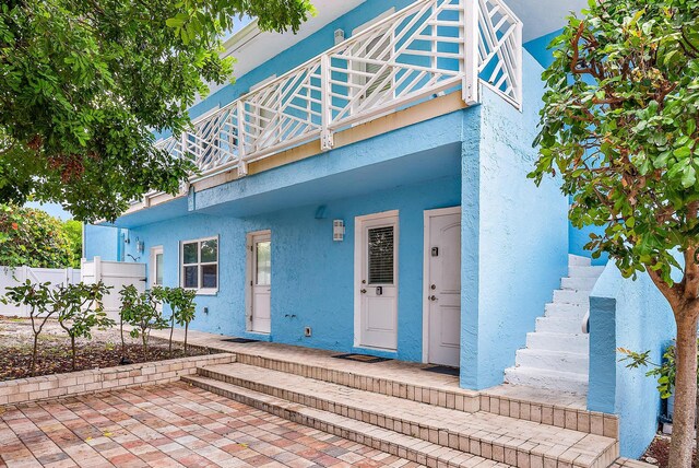 view of front facade featuring stairs, fence, a balcony, and stucco siding