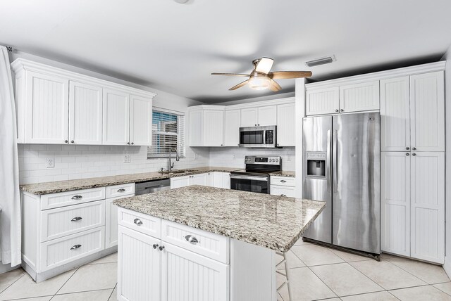 kitchen featuring stainless steel appliances, light tile patterned flooring, a kitchen island, and white cabinets