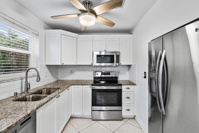 kitchen featuring light tile patterned floors, stainless steel appliances, stone counters, white cabinetry, and a sink