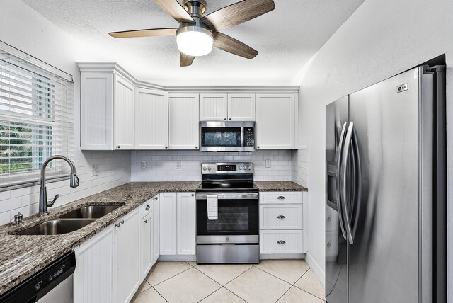 kitchen with appliances with stainless steel finishes, dark stone countertops, a sink, and white cabinets