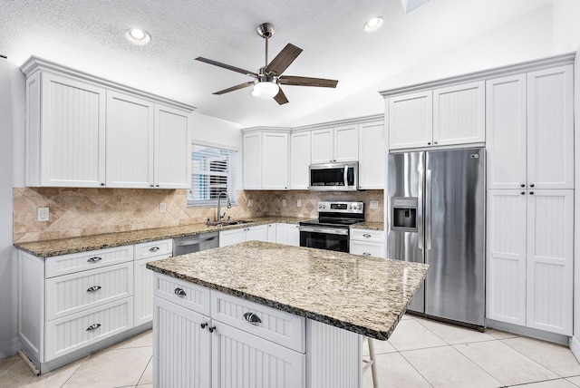 kitchen featuring a kitchen island, light stone counters, appliances with stainless steel finishes, vaulted ceiling, and a sink