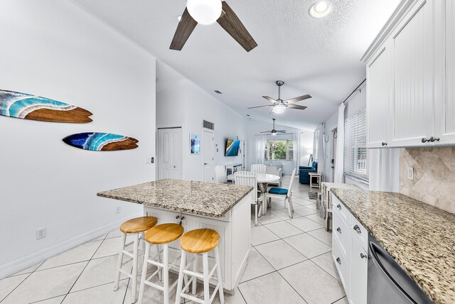 kitchen with a kitchen island, a kitchen breakfast bar, white cabinets, light stone countertops, and dishwasher