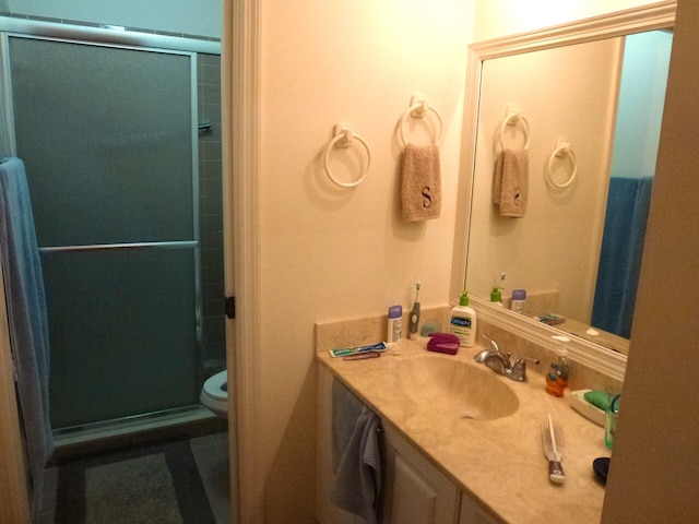 bathroom featuring a shower with door, toilet, and vanity