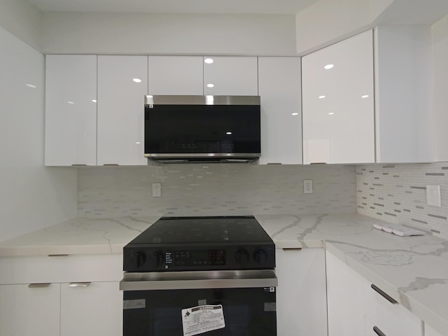 kitchen with stainless steel range with electric cooktop, white cabinets, light stone countertops, and decorative backsplash