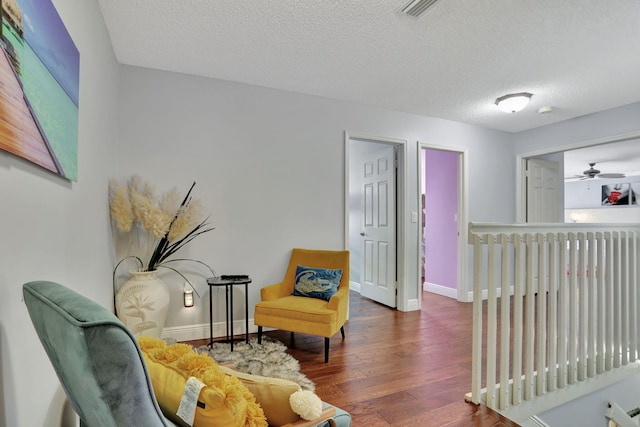 living area featuring ceiling fan, dark wood-type flooring, and a textured ceiling