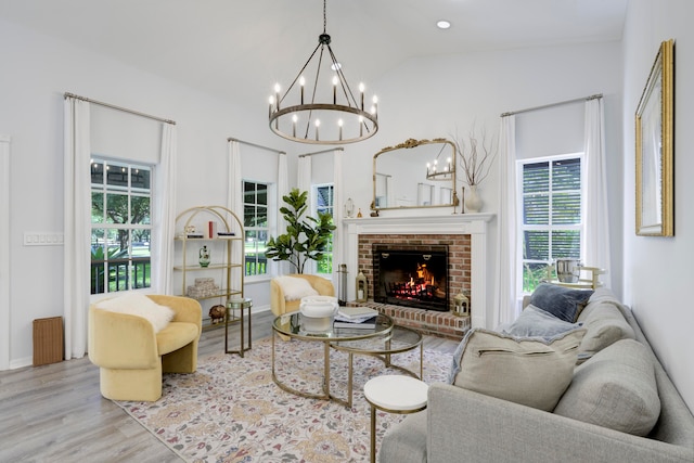 living room with light wood-type flooring, a fireplace, a chandelier, and vaulted ceiling