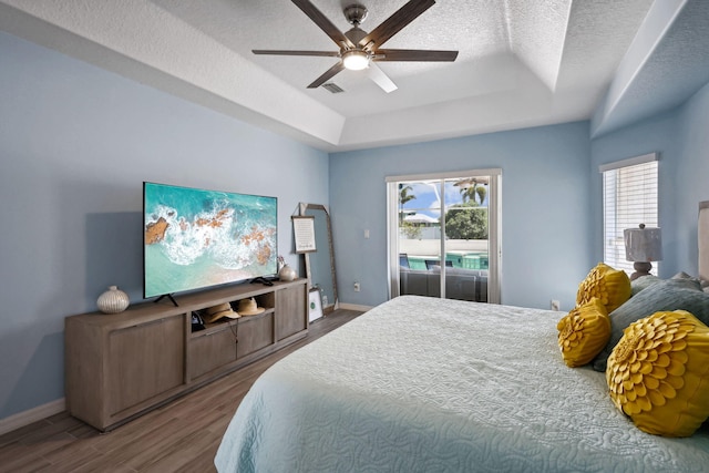 bedroom featuring ceiling fan, access to outside, a tray ceiling, hardwood / wood-style floors, and a textured ceiling